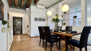 Un coin repas avec une table en bois, des chaises noires et une cloison en verre. On peut y voir des tableaux encadrés au mur, un vase avec des fleurs et un luminaire suspendu.