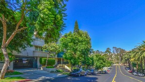 A street lined with trees and parked cars, leading to a building with a sign that reads "Hotel."