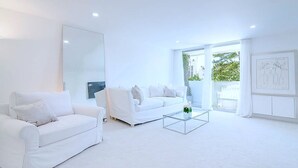 A spacious, modern living room with white furniture and large windows.