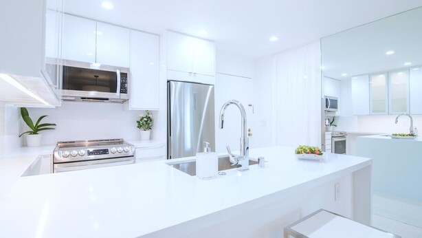A modern kitchen with stainless steel appliances, white cabinetry, and a central island with a sink.