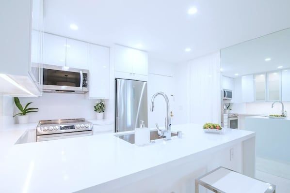 A modern kitchen with stainless steel appliances, white cabinetry, and a central island with a sink.