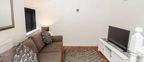 A living room with a brown sofa, a television on a white stand, a pebbled floor rug, and a painting on the wall.