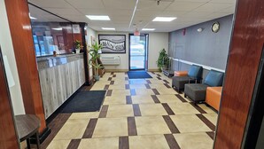 Un área de recepción con mostrador de check-in, una sala de espera con asientos, piso de baldosas y un reloj en la pared.