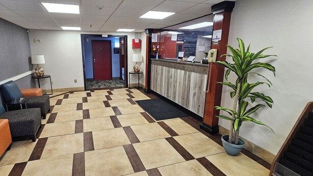 Un vestíbulo de hotel con mostrador de recepción, un reloj, una planta en maceta y zonas de estar.
