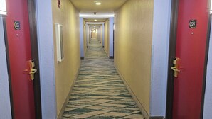 Un pasillo de hotel con puertas rojas, letreros de habitaciones numeradas y una alfombra estampada.
