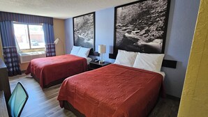 Habitación de hotel con dos camas, un escritorio, una silla, un ventanal con cortinas y dos lámparas de pared.
