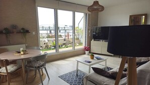 A modern living room with a dining area, large windows, and a painting on easel.