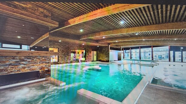 An indoor swimming pool with a stone wall and wooden ceiling.
