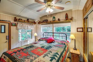 Une chambre à coucher avec un grand lit, deux fenêtres, un ventilateur de plafond et une étagère en bois au-dessus du lit.