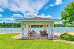 A gazebo with a tiled roof and lattice sides, surrounded by a grassy area and a body of water. - Steps to Smith Mountain Lake: Unit w/ Pool Access! (Huddleston)
