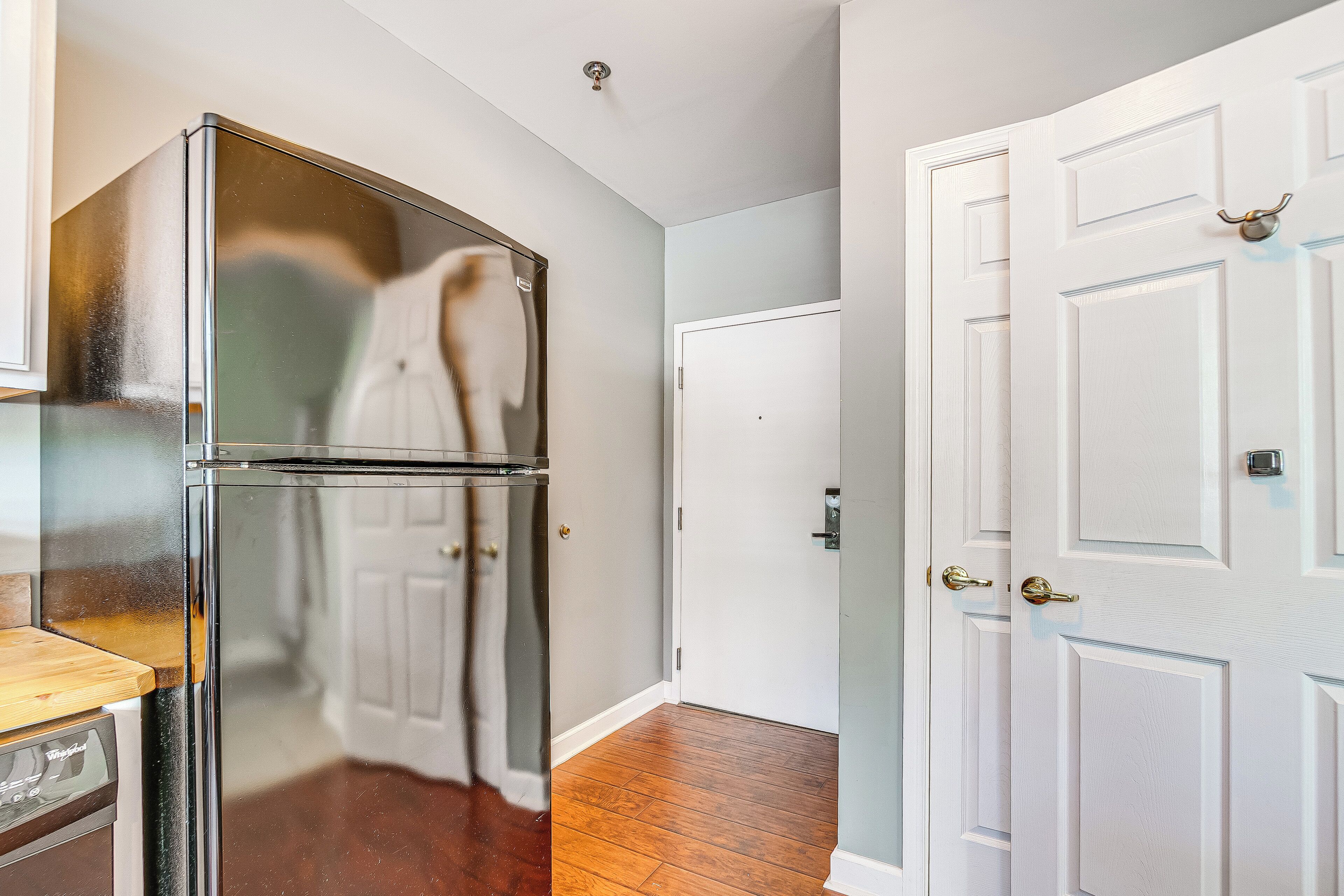 A kitchen with a stainless steel refrigerator, a wooden countertop, and a white door with a brass handle.