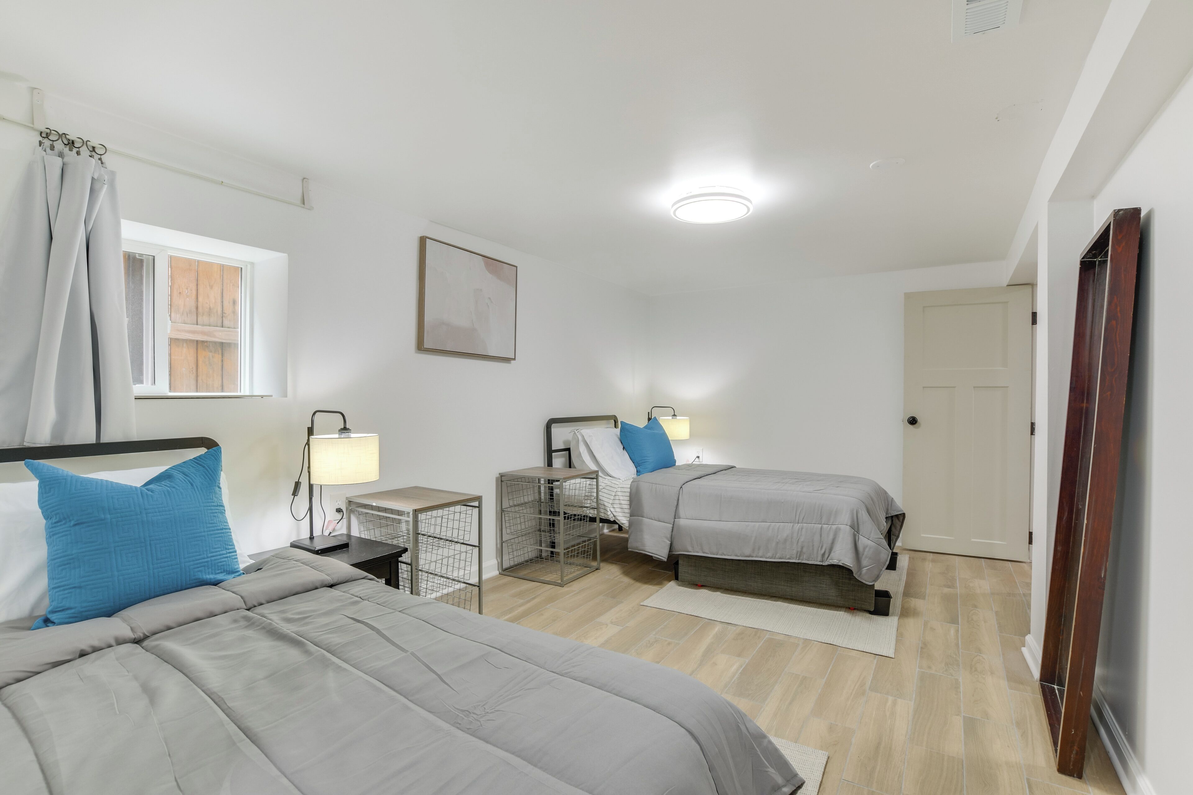 Un dormitorio con dos camas, una mesita de noche con lámpara, un escritorio pequeño y una ventana con cortinas.