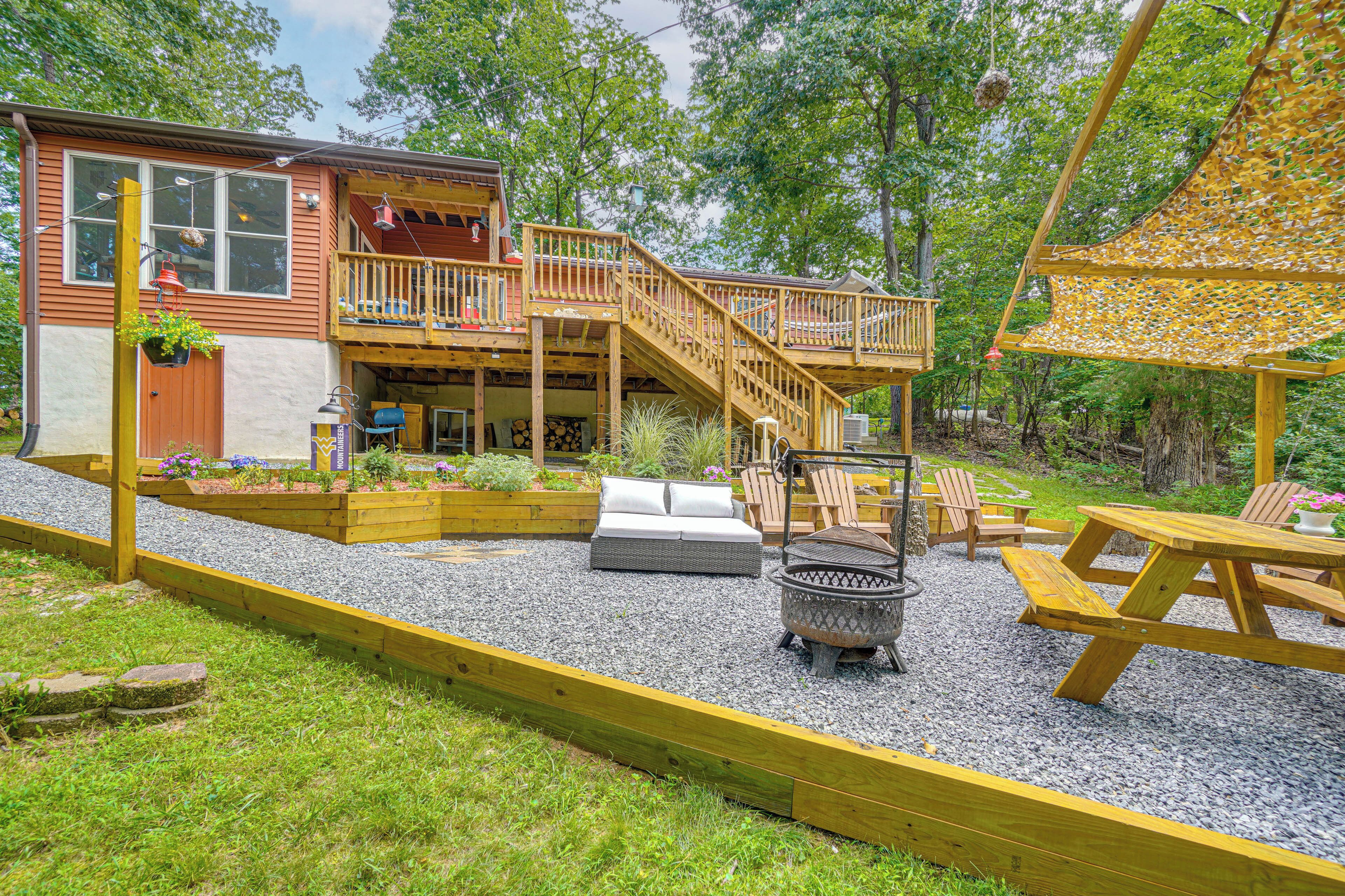 A wooden deck with a staircase leading to a balcony, surrounded by a gravel area with outdoor furniture.