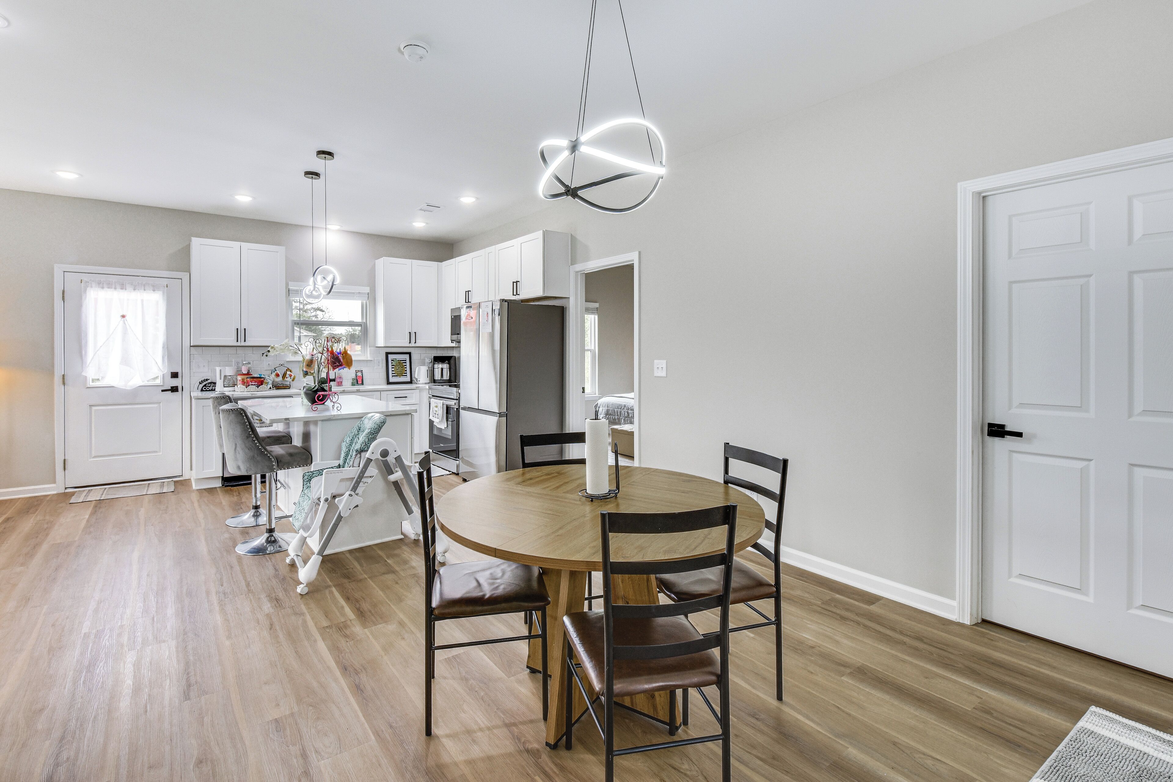 Una cocina moderna con armarios blancos, una mesa de comedor de madera y una lámpara colgante.