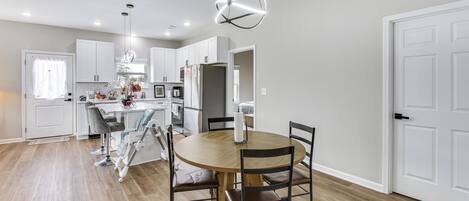 Una cocina moderna con armarios blancos, una mesa de comedor de madera y una lámpara colgante.