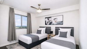 A hotel room with two beds, a ceiling fan, a window with curtains, and a framed picture on the wall. - Stylish Townsville CBD Apartment with Pool, Parking & Balcony (Townsville City)