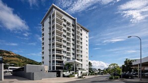 A modern multi-story hotel with balconies, a parking area, and a clear sky. - Stylish Townsville CBD Apartment with Pool, Parking & Balcony (Townsville City)