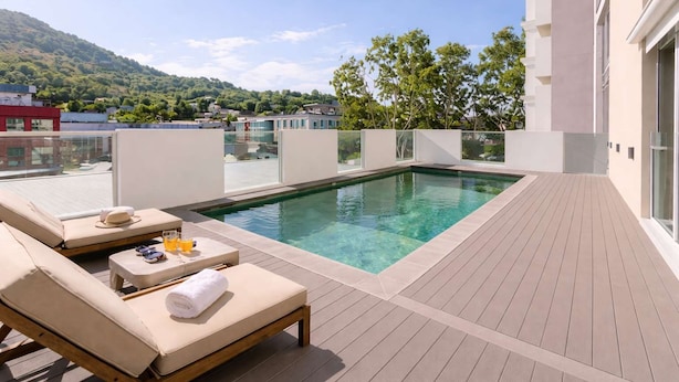 A rooftop pool with lounge chairs, a glass balustrade, and a view of a green hillside. - Stylish Townsville CBD Apartment with Pool, Parking & Balcony (Townsville City)