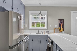 A kitchen with a stainless steel refrigerator, a double sink, and a window with blinds.