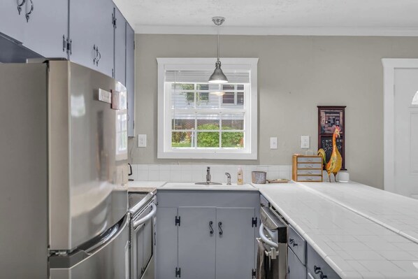 A kitchen with a stainless steel refrigerator, a double sink, and a window with blinds.