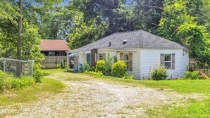 A single-story house with a front porch, a fenced yard, and a gravel driveway. - Cozy Spot - Perfect for Long Stays - Walk Downtown (Spartanburg)