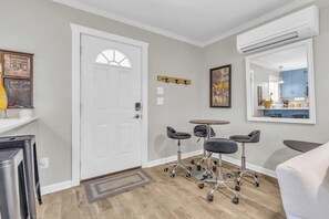A room with a white door, a small table with four chairs, a coat rack, and a large mirror on the wall.