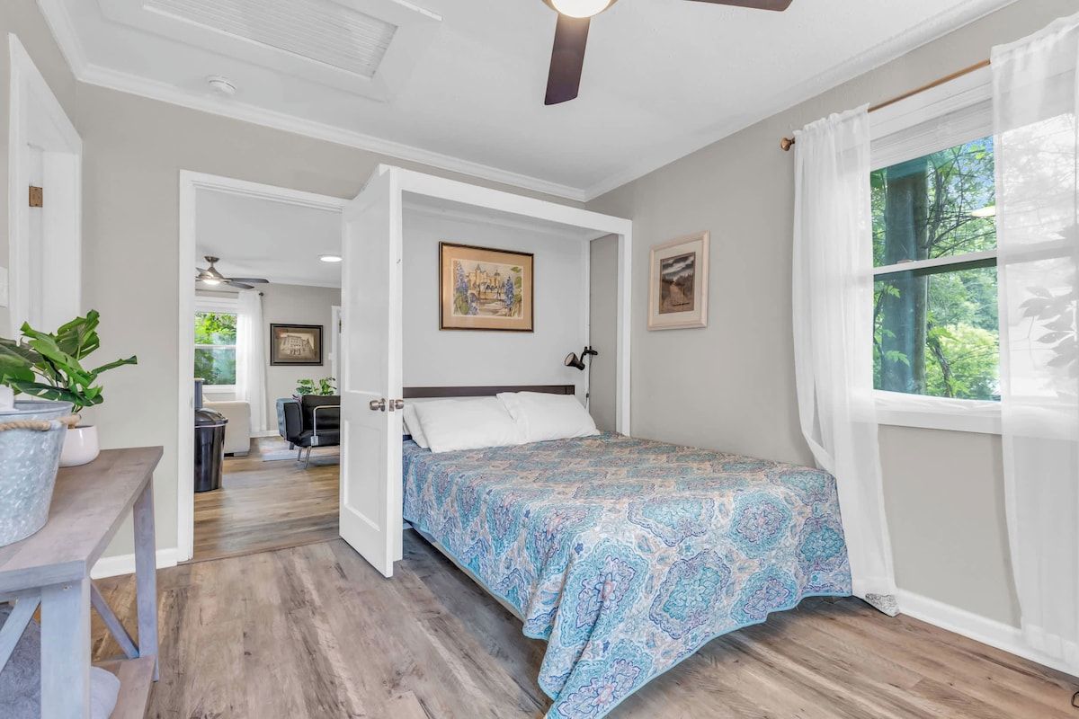 Un dormitorio con cama, ventilador de techo y ventana con cortinas.