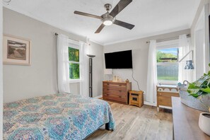A bedroom with a bed, a ceiling fan, a dresser, a TV, and a window with curtains.