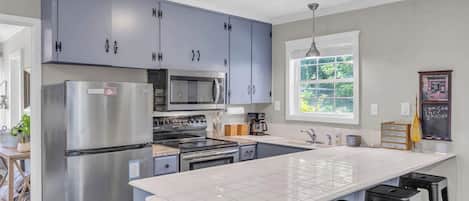 Una cocina moderna con armarios grises, electrodomésticos de acero inoxidable, una isla grande y taburetes de bar.