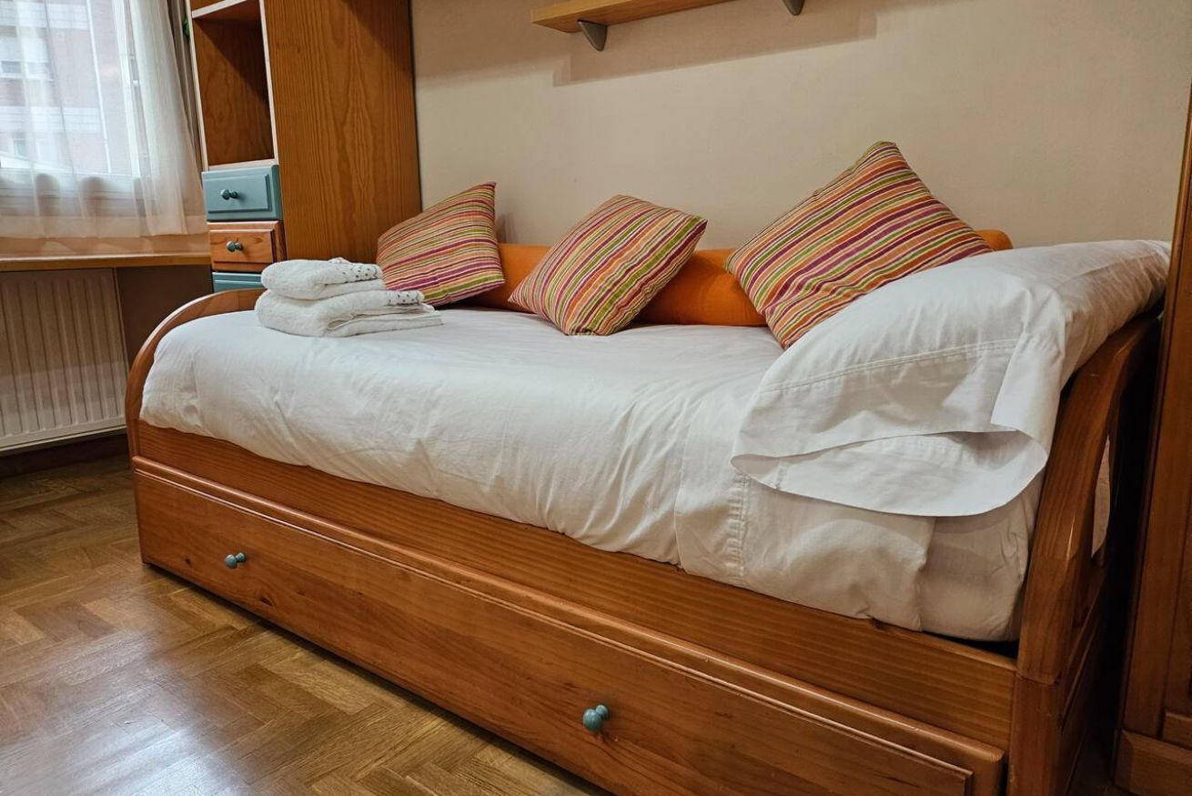 Uma cama de madeira com lençóis brancos, almofadas listradas e uma mesa de cabeceira de madeira com gavetas.
