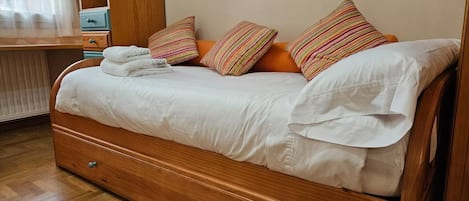 A wooden bed with white linens, striped pillows, and a wooden nightstand with drawers.