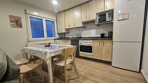 A compact kitchen with wooden cabinets, a Bosch refrigerator, a microwave, and a dining table with chairs. - 1A111 Apartamento moderno de 3 dormitorios. (Gijón)