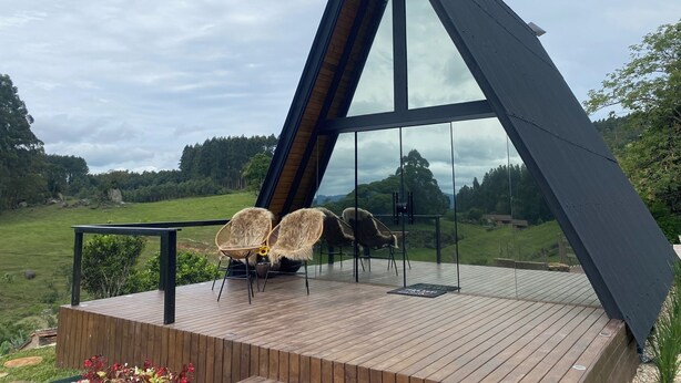 A modern, triangular glass structure with a wooden deck and two wicker chairs. - Miraflores Recanto (Imarui)