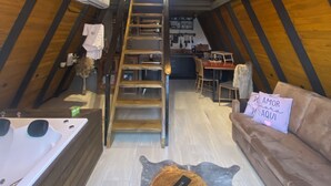 A cozy attic bedroom with a wooden sloped ceiling, a central staircase, a wooden dining table, and a sofa with a cushion. - Miraflores Recanto (Imarui)