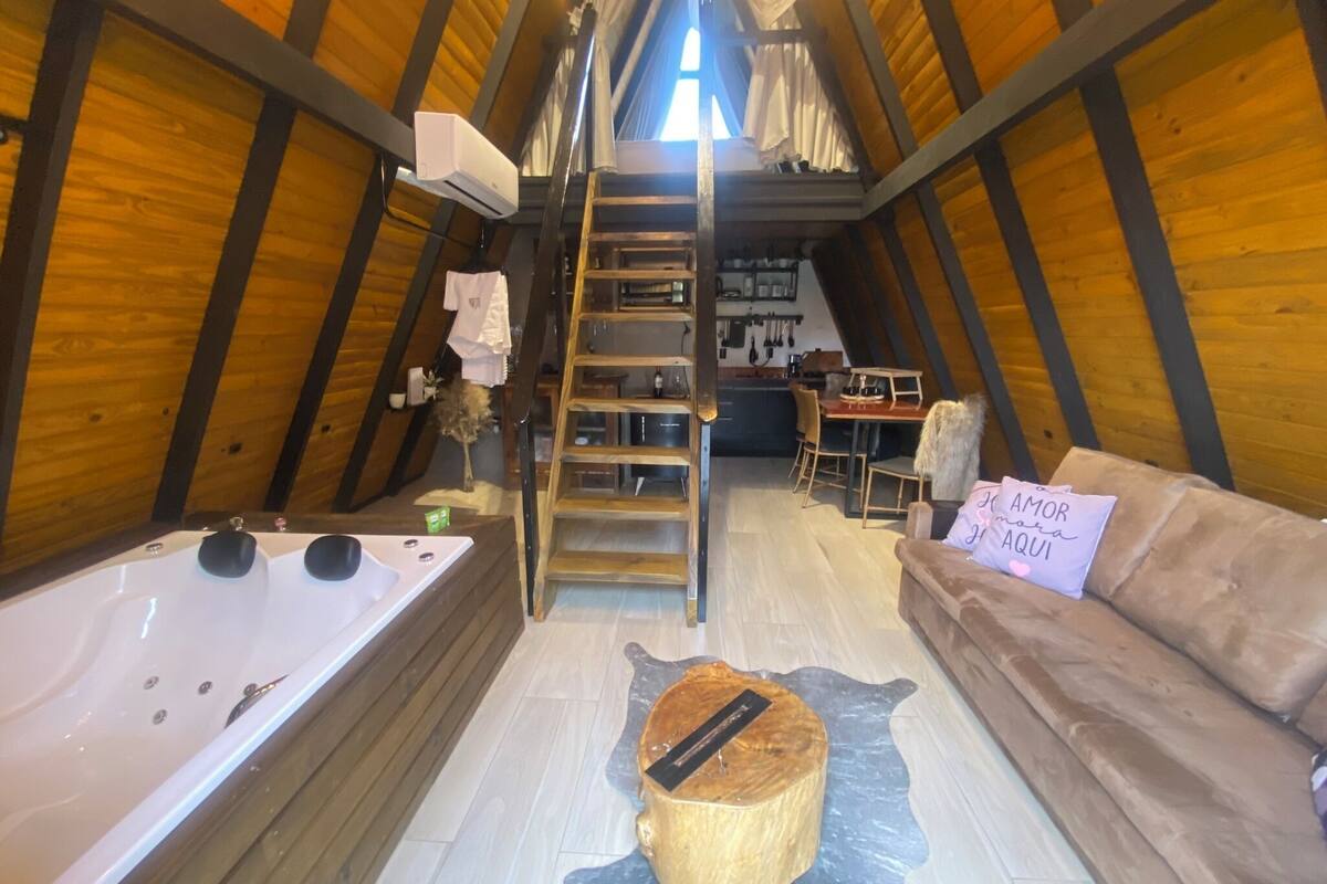 Ein Schlafzimmer im Dachgeschoss mit schrägen Holzwänden, einer Holzleiter, einer Badewanne, einem hölzernen Hocker, einem Sofa und einem Schild mit einer Botschaft.