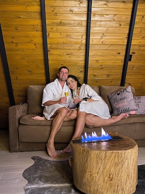 Et par slapper af på en sofa i et rum med trævægge og et lille træbord med en blå flamme.