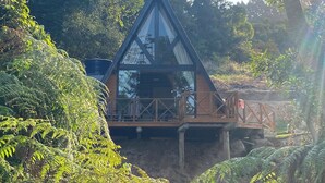 A wooden cabin with a triangular roof, surrounded by dense greenery. - Miraflores Recanto (Imarui)