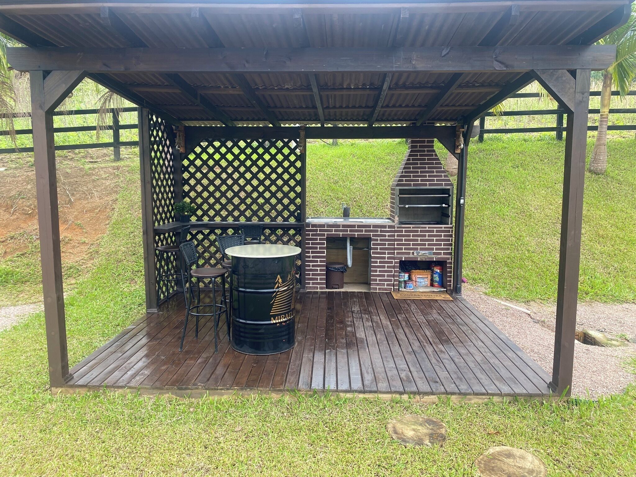 Zona de barbacoa al aire libre con horno de ladrillo, parrilla y área de estar con sillas y una mesa.