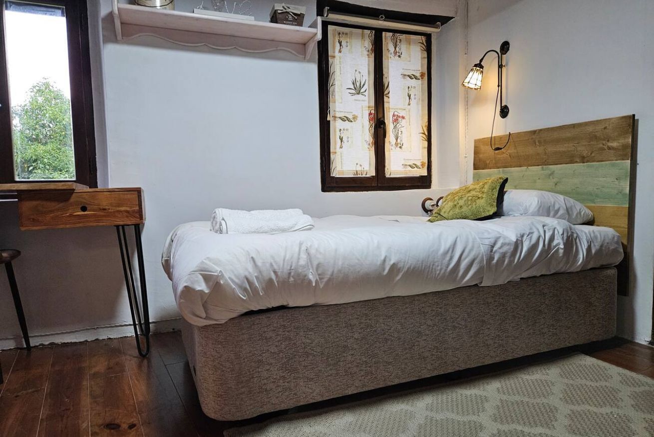 A bedroom with a bed, a window with curtains, a bedside lamp, and a wooden headboard.
