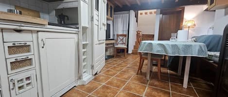 A kitchen with white cabinets, a dining table with a tablecloth, and a chair.