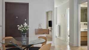 A modern dining area with a glass table and wooden chairs, a dark wooden door, and a wall-mounted TV. - Athens Glow 2bd Apt in Ilisia (Athina)