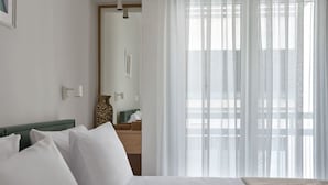 A hotel room with a bed, a bedside table, a mirror, and sheer curtains. - Athens Glow 2bd Apt in Ilisia (Athina)