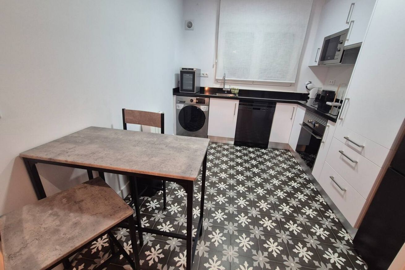 Cocina compacta equipada con lavadora, microondas y un pequeño comedor con mesa y sillas.