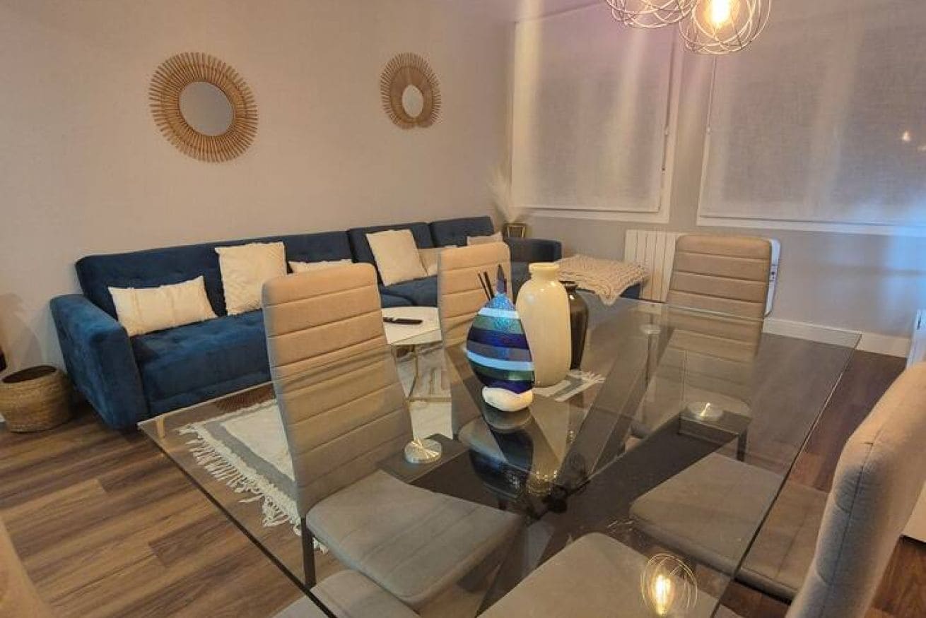 A modern living room with a glass dining table, sofas, and decorative wall mirrors.