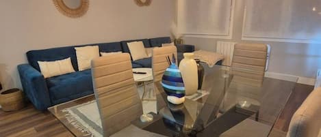 A modern living room with a glass dining table, sofas, and decorative wall mirrors.