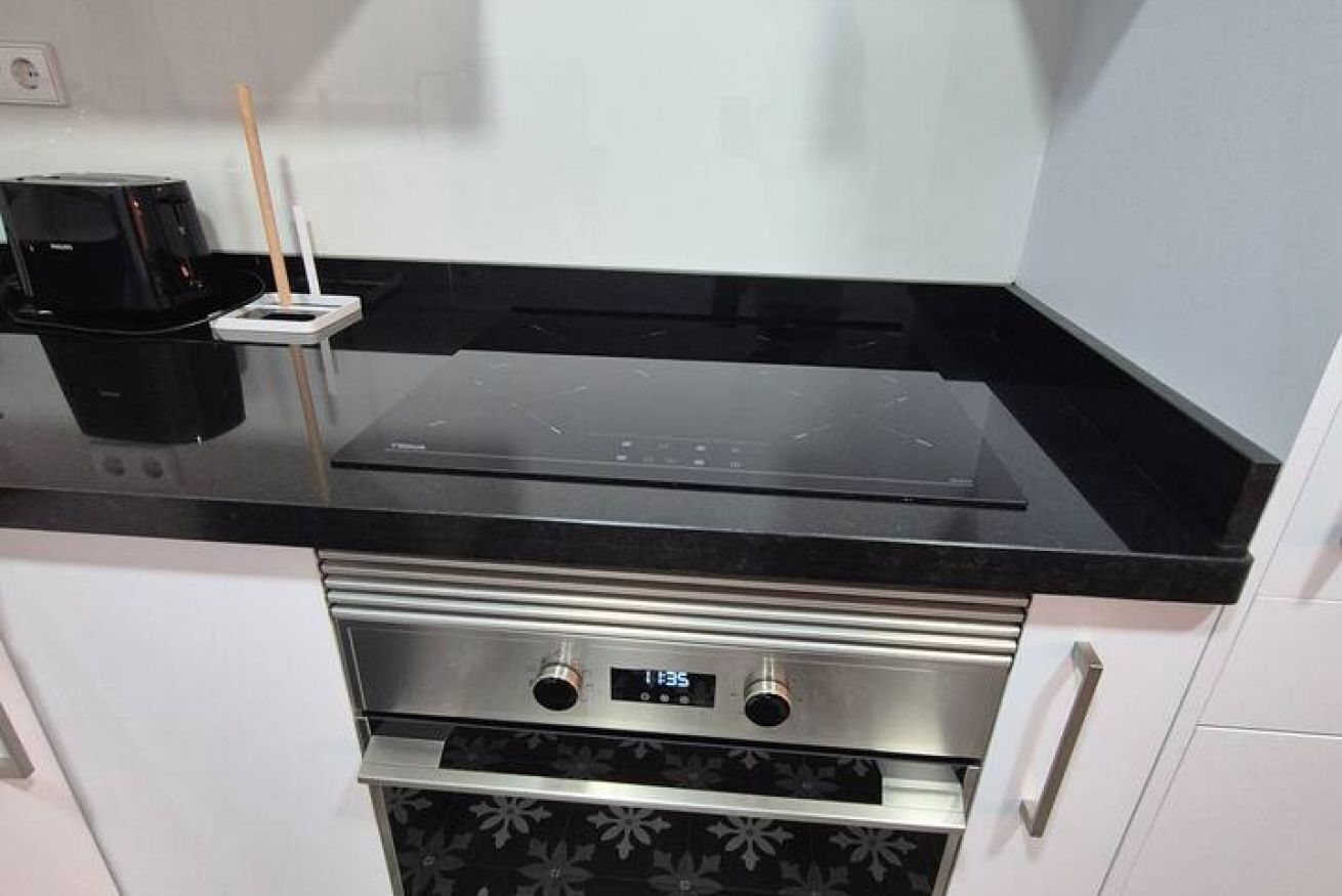 Una cocina con encimera negra, una cafetera y un reloj digital que muestra las 11:35.