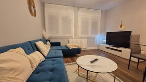 Una sala de estar con un sofá azul, una mesa de centro redonda, un televisor y una silla.