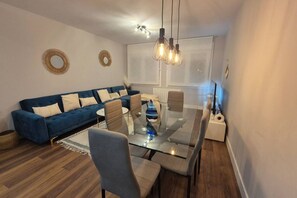 A modern living room with a glass dining table, blue sofa, and a white radiator. - 1A136 Mar de Poniente (Gijón)
