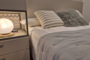 A neatly made bed with a striped pillow, a fluffy pillow, and a bedside lamp on a nightstand.