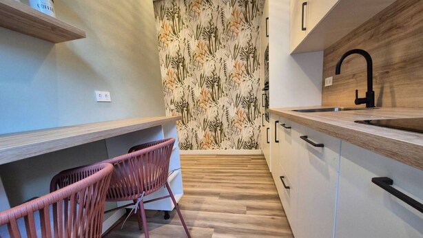 A modern kitchen with wooden cabinets, a black faucet, and a patterned wallpaper.